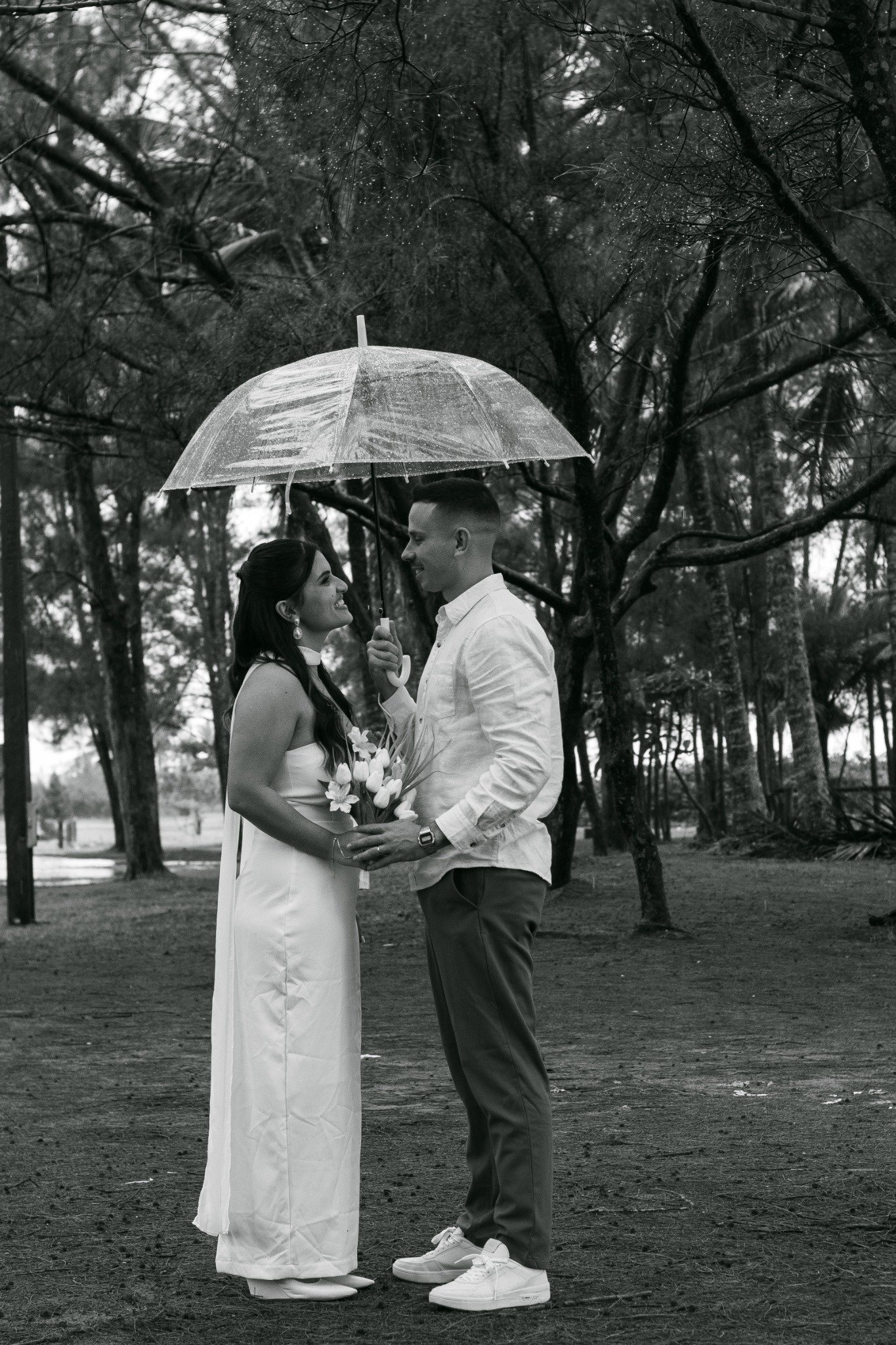 Gabriella e Gustavo juntos sob um guarda-chuva entre as árvores.