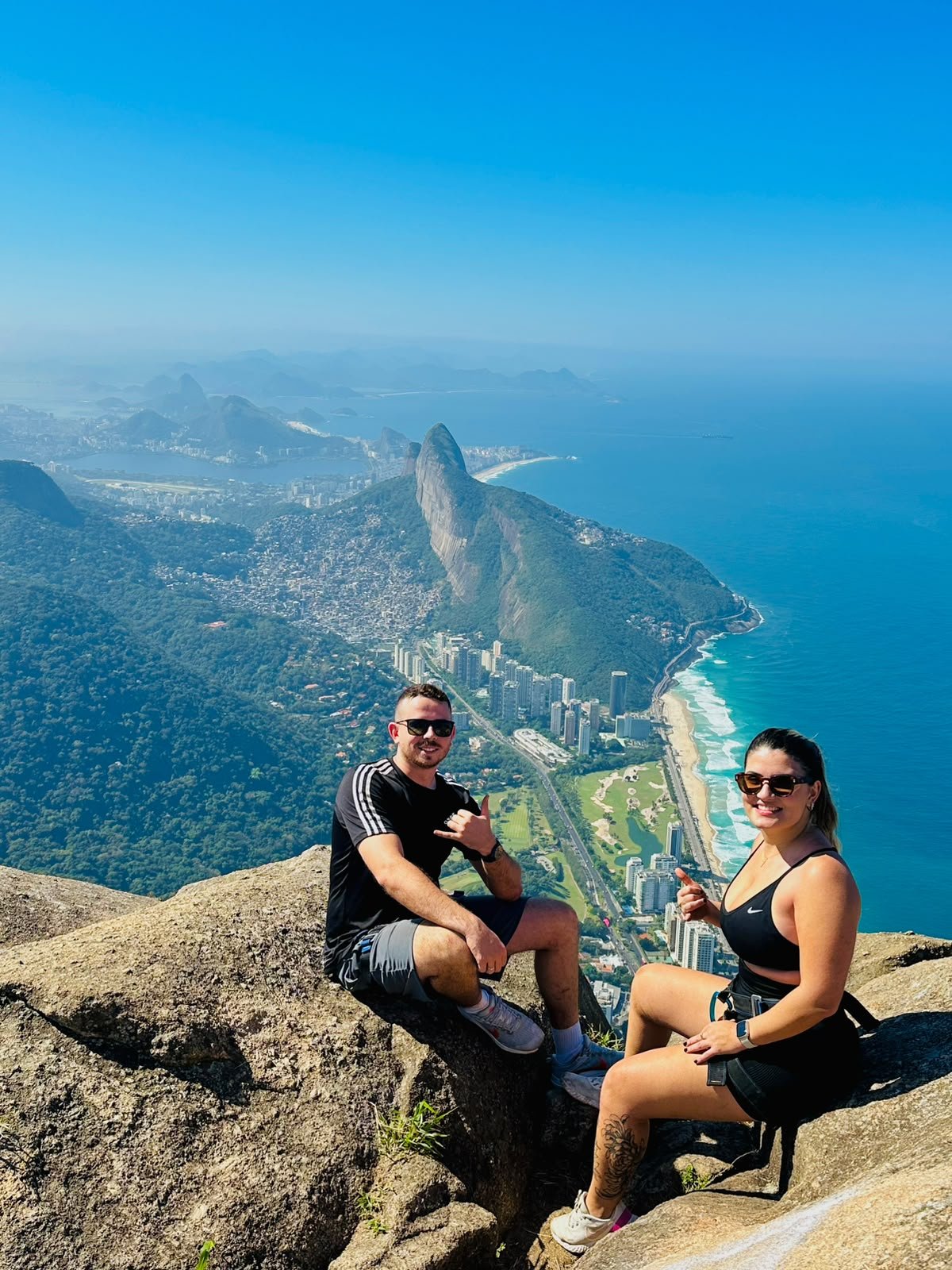 O casal em uma trilha com vista para o mar e as montanhas do Rio de Janeiro.