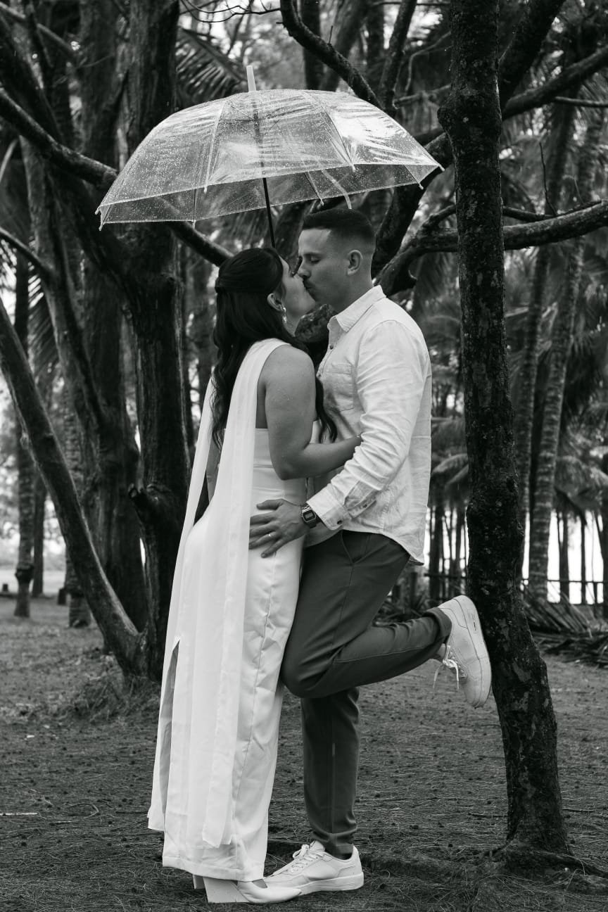 O casal se beijando sob um guarda-chuva transparente.