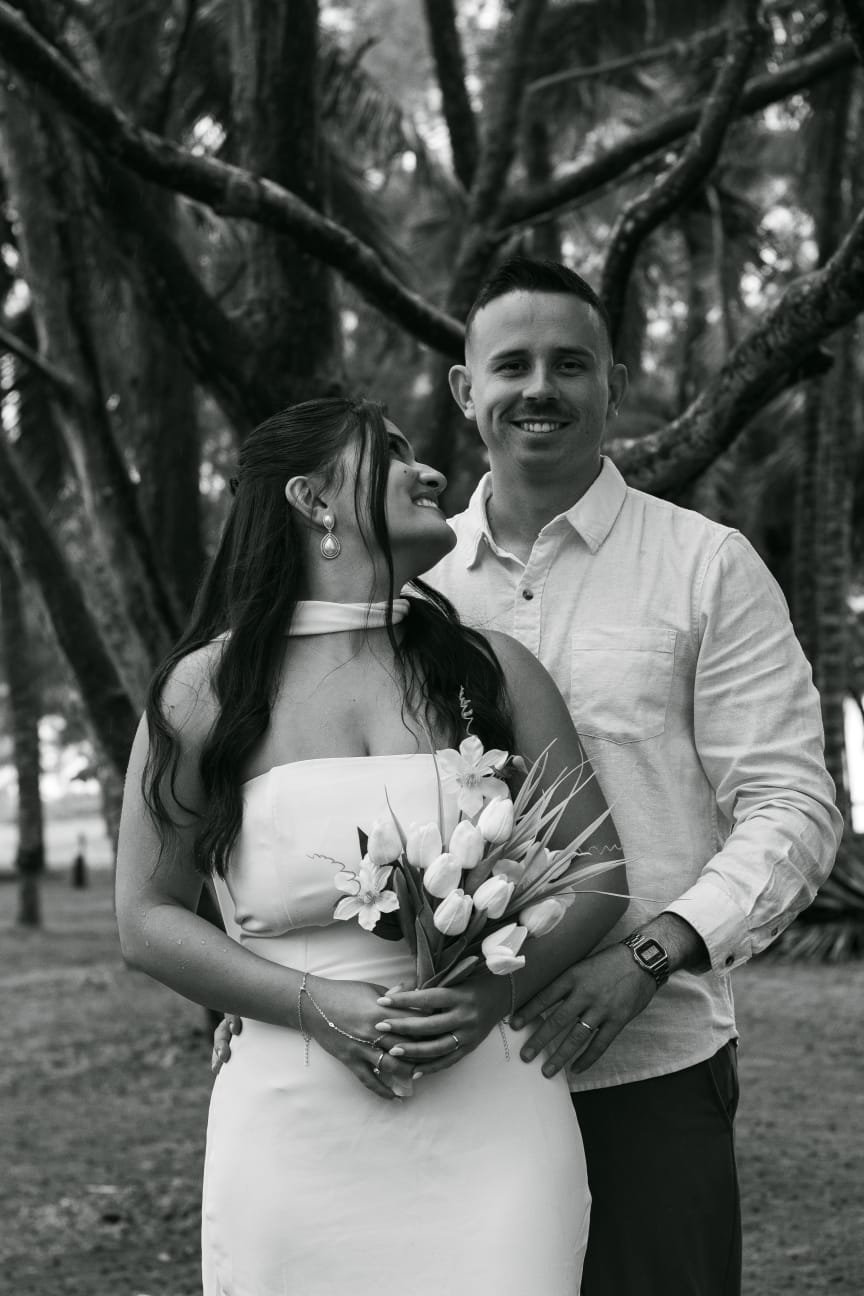 Gabriella com o buquê ao lado de Gustavo entre as árvores.